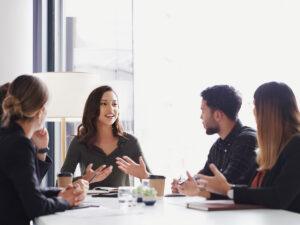 A diverse group of people engaged in conversation around a table, sharing ideas and collaborating in a meeting setting.