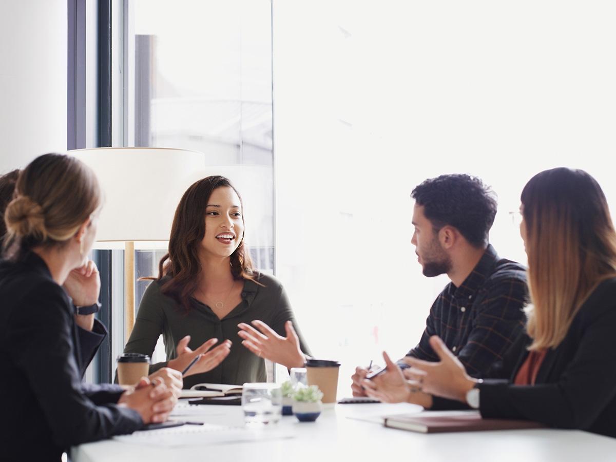 A diverse group of people engaged in conversation around a table, sharing ideas and collaborating in a meeting setting.